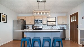 Una cocina moderna con una isla central, electrodomésticos de acero inoxidable y taburetes de bar azules.
