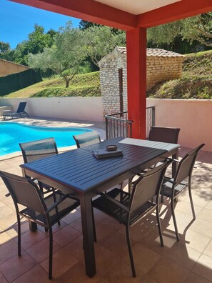 Une terrasse extérieure avec une piscine, un mur en pierre et une table entourée de chaises.