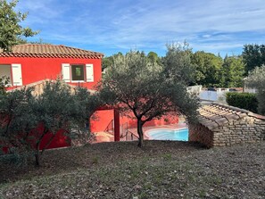 Un bâtiment rouge avec un toit en tuiles, un pont de pierre et une piscine.