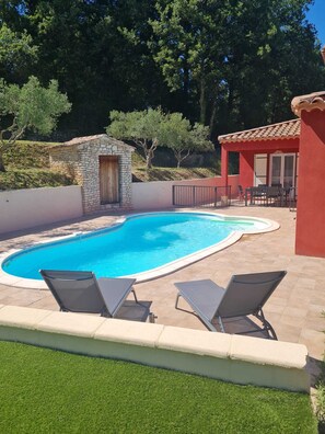 Une piscine avec deux chaises longues, une structure en pierre et un bâtiment rouge avec un toit en tuiles.