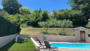 A backyard with a swimming pool, lounge chairs, and a stone wall.