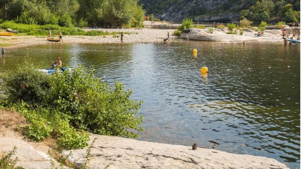 A river with boats, people, and a rocky cliff in the background.