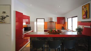 Una cocina moderna con armarios rojos, una isla central con taburetes y un gran ventanal que proporciona luz natural.