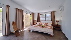 Un dormitorio con una cama grande, una silla de madera, una mesita de noche y una ventana con cortinas.