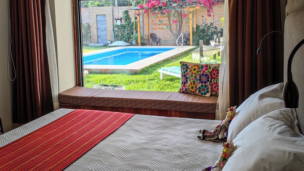 Un dormitori amb una finestra gran, un llit, una taula de nit i vista a una piscina i un jardí.