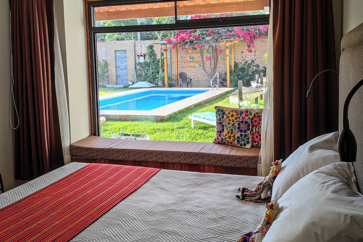 Un dormitorio con un ventanal grande, una cama, una mesita de noche y vistas a una piscina y jardín.