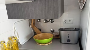 Een compacte keuken met een broodrooster, een groene kom en twee gele glazen op een aanrecht.