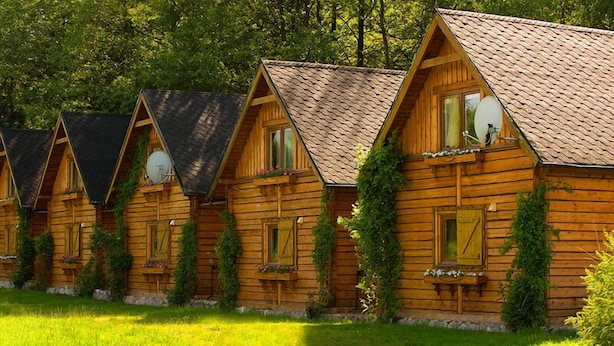 A row of wooden cabins with pitched roofs, each featuring a window with shutters and a small porch area. - Przystan Apartamenty Hotel  (Myslakowice)