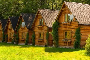 A row of wooden cabins with pitched roofs, each featuring a window with shutters and a small porch area. - Przystan Apartamenty Hotel  (Myslakowice)