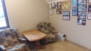 A corner room with a wooden table and two patterned armchairs, a radiator, and a wall adorned with framed photos and certificates. - Przystan Apartamenty Hotel  (Myslakowice)