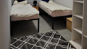 A small, well-lit room with two single beds, a nightstand with a lamp, a large painting on the wall, and a wardrobe. - Przystan Apartamenty Hotel  (Myslakowice)