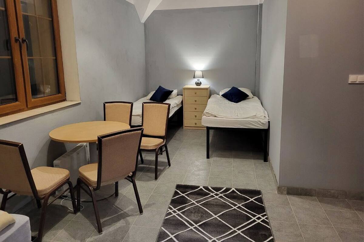 Ein kleiner, kompakter Raum mit einem Bett, einem Tisch mit Stühlen, einer Lampe und einem Heizkörper.