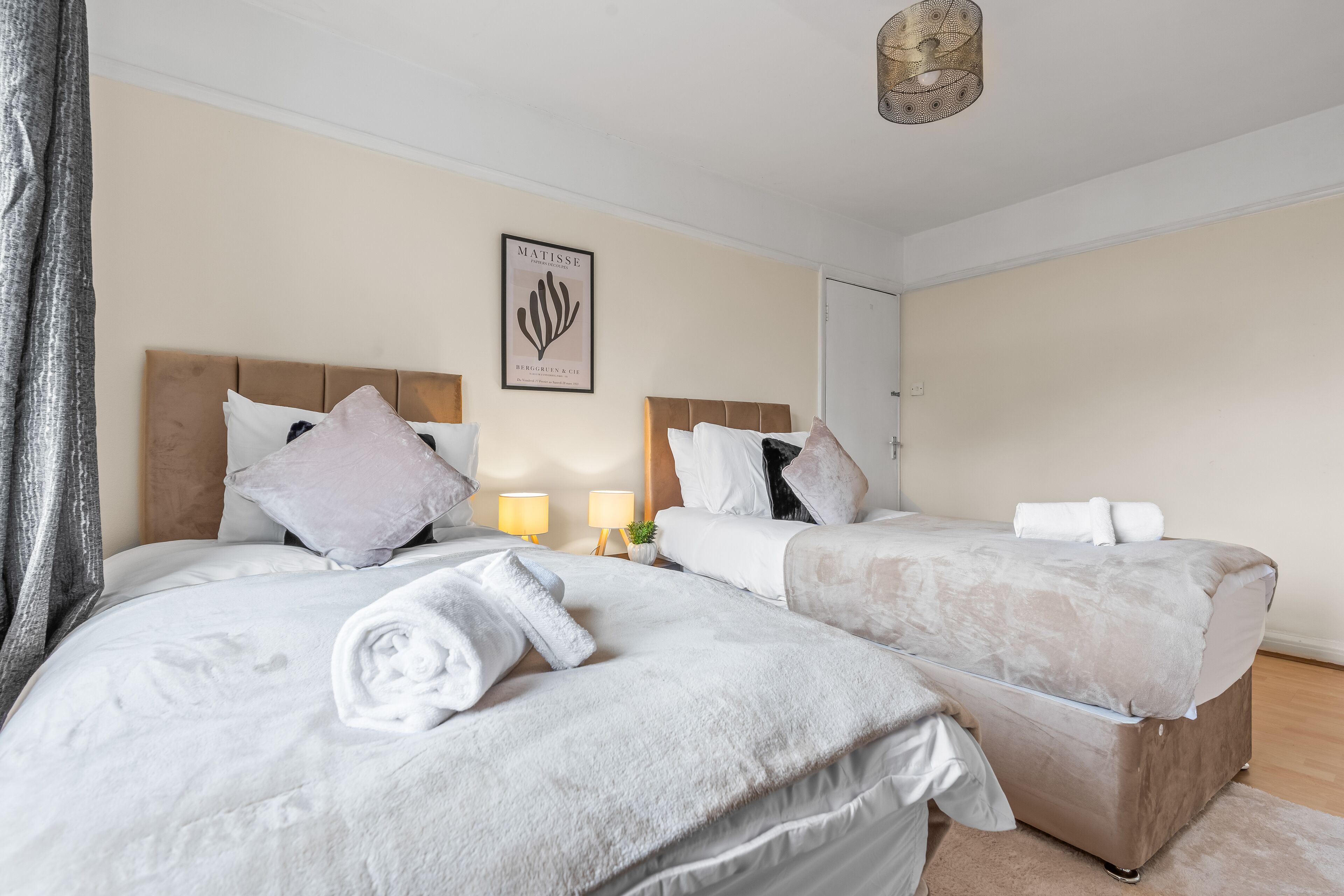 A hotel room with two beds, a framed artwork on the wall, and a bedside lamp.
