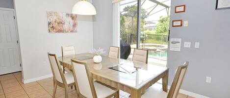 A dining area with a wooden table and chairs, a pendant light, a window with a view, and a wall with framed pictures and a certificate.