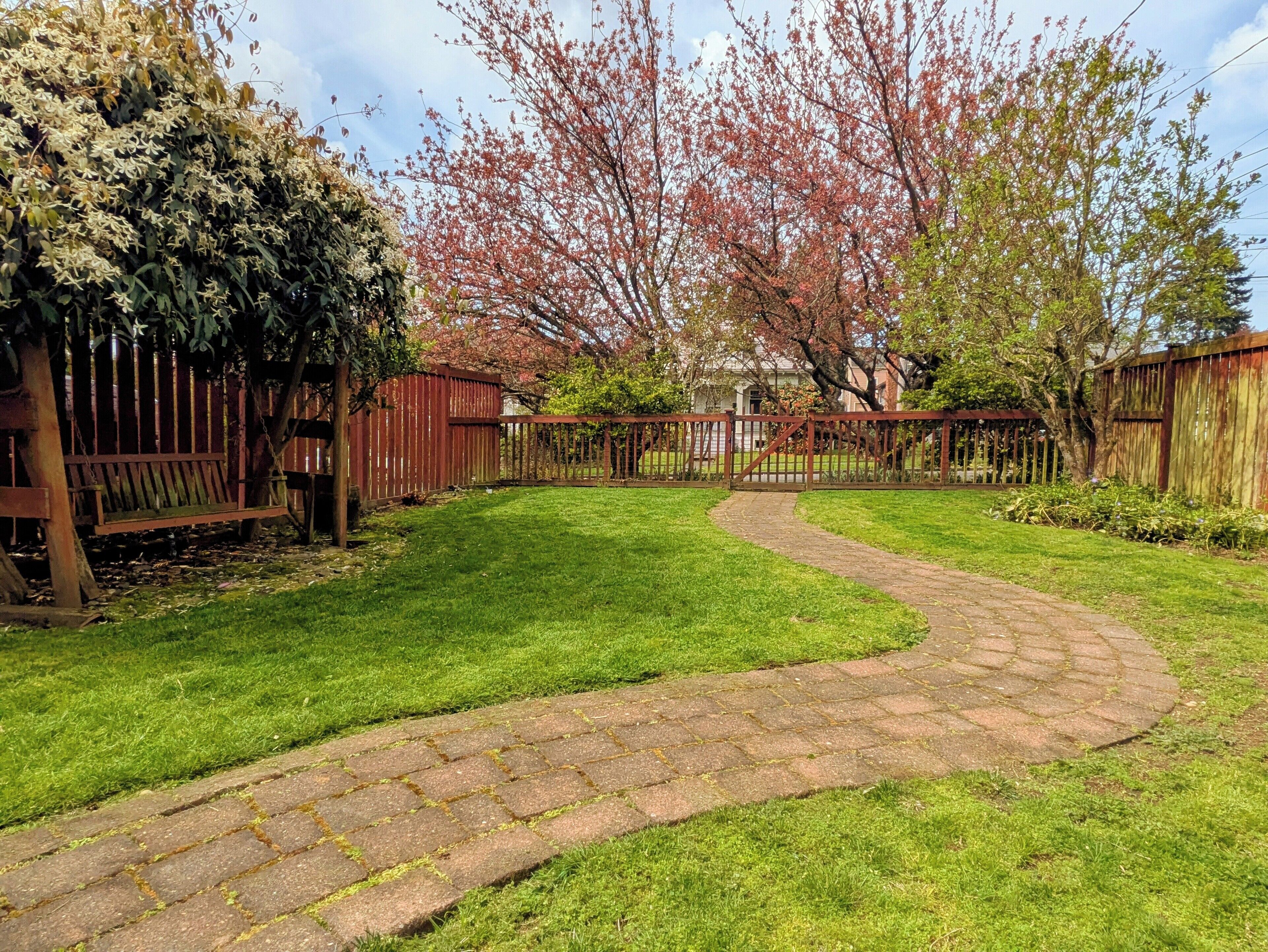 A paved pathway leading to a house with a wooden fence and a bench.