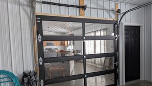 Een garage met een grote zwarte deur, een balkenplafond en een betonnen vloer.