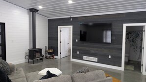Een moderne woonkamer met een open haard, een grote flatscreen televisie en een grijze bank.