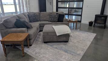 A modern living room with a sectional sofa, a small ottoman, a wooden coffee table, and a large window with curtains.