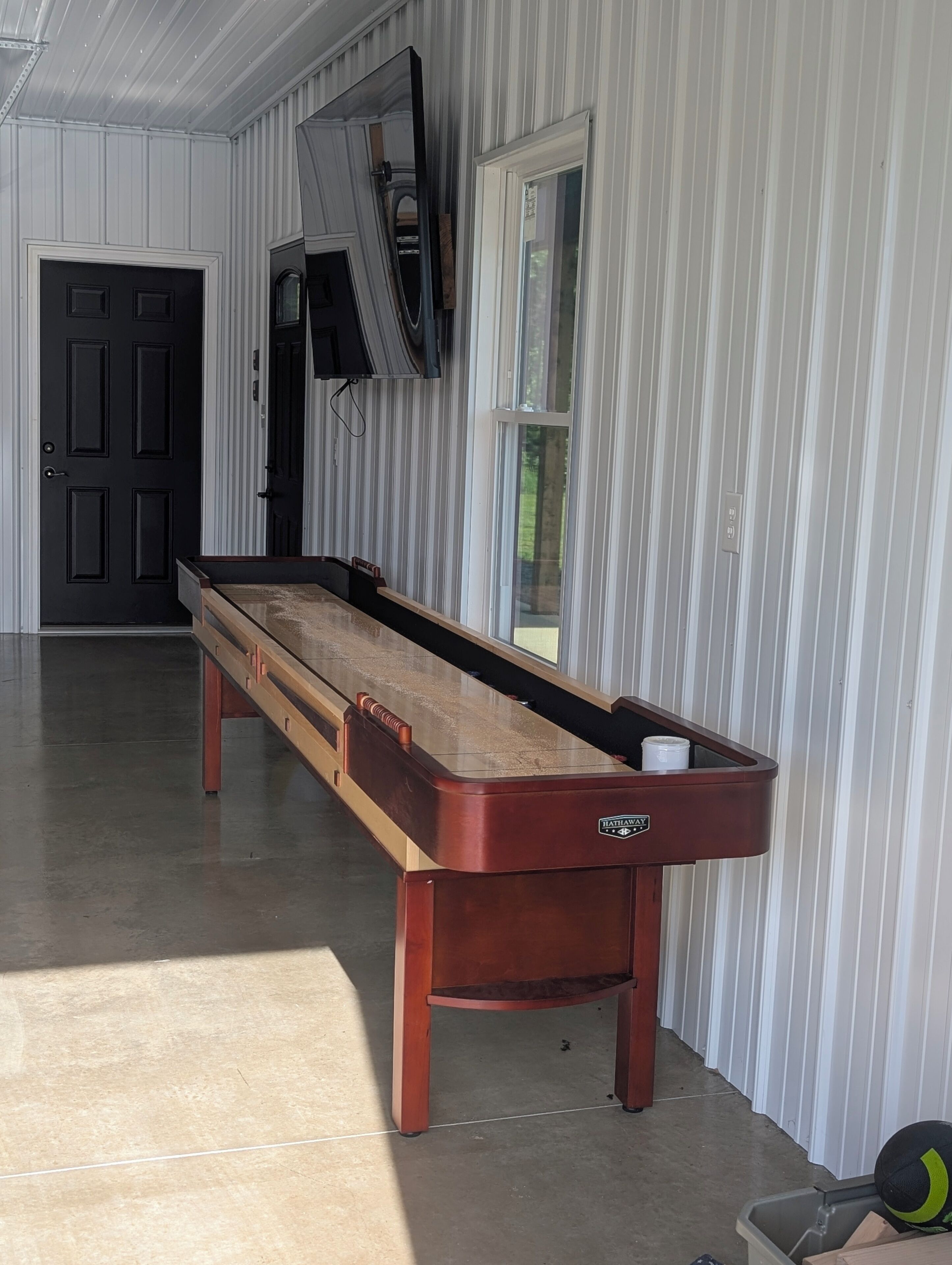 Une table de billard dans une pièce dont un mur est rayé, avec une porte et un téléviseur fixé au mur.