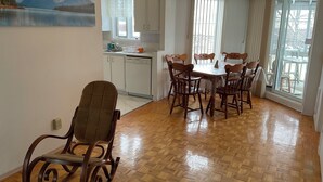 A dining area with a wooden table and chairs, a kitchen with white cabinets, and a large window with curtains. - Family-Friendlyin QuietLaval Neighborhood (Laval)