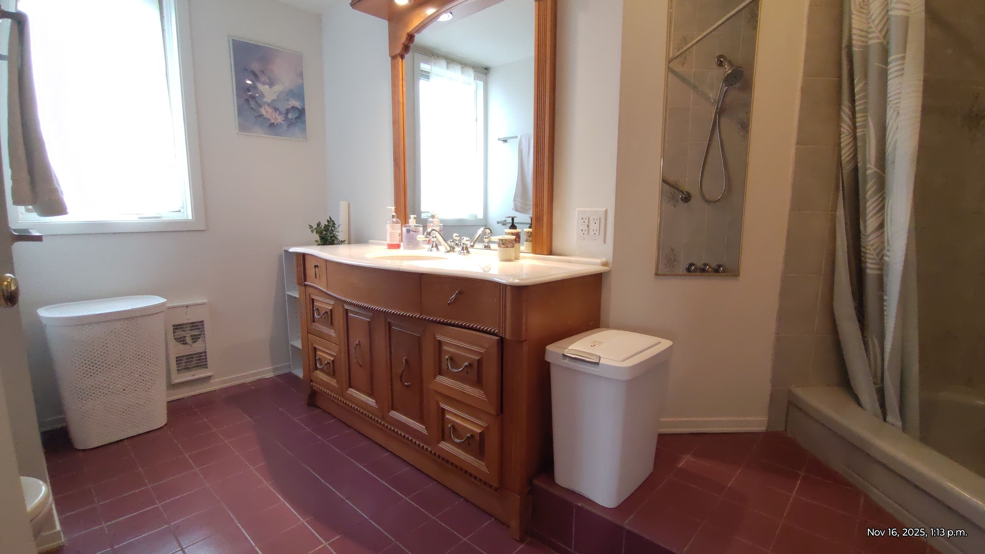 Une salle de bain avec un meuble-lavabo en bois, des toilettes blanches, une douche avec une porte en verre et une fenêtre donnant sur le ciel.