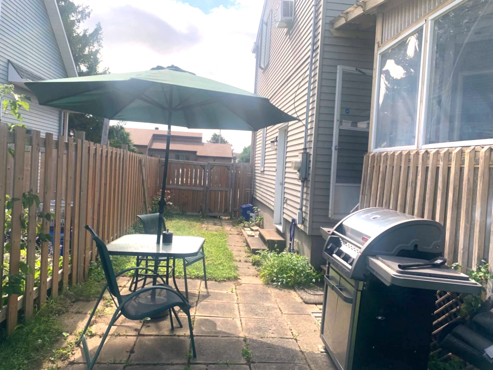 Un jardin avec une table et des chaises de patio, un barbecue et une clôture en bois.