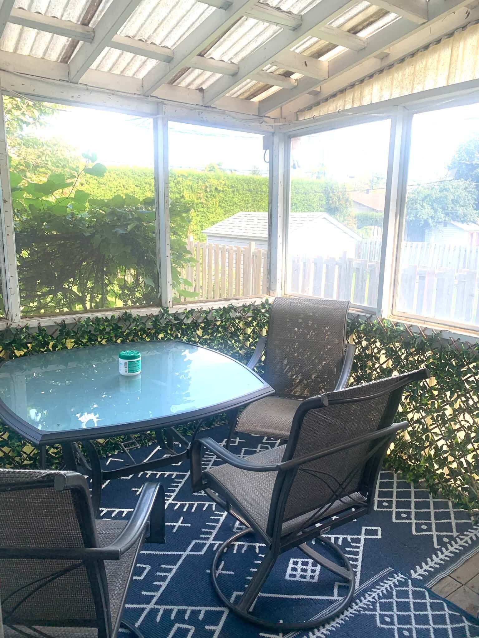 Un patio techado con mesa y sillas, ventanas amplias y vista a la vegetación.