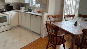 A kitchen with white cabinets, a stove, a sink, and a dining table with chairs. - Family-Friendlyin QuietLaval Neighborhood (Laval)