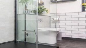 Une salle de bain moderne avec une douche à l’italienne en verre, des carreaux blancs et des toilettes blanches.