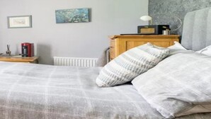 Une chambre à coucher avec un lit, des oreillers, une table de chevet avec une lampe, une radio et un tableau encadré au mur.