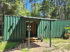 A green metal structure with a wooden bench and potted plants in front. - Rustic Glamping with Goats in Forest Near Houston (Cleveland)