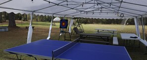 An outdoor pavilion with a ping pong table, picnic tables, and a target for archery. - Rustic Glamping with Goats in Forest Near Houston (Cleveland)