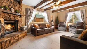 Een gezellige woonkamer met een stenen openhaard, een bruine leren bank en een houten plafond.