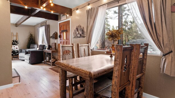 Een rustieke eethoek met een houten tafel en stoelen, een houten bank en een uitzicht op het omliggende landschap door grote ramen.