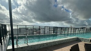 Una piscina en la azotea con vistas al horizonte de la ciudad y nubes en el cielo.