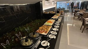 Zona de bufé con diversas opciones de comida, una estufa con ollas y un área de descanso con mesas y sillas.