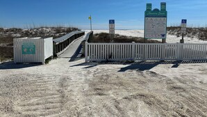 A beach access walkway with informational signs, a trash disposal bin, and a white fence. - The Retreat at Sunset Harbor (Navarre)