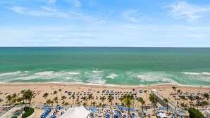 A beach resort with rows of sun loungers and umbrellas, a pool area, and a view of the ocean.