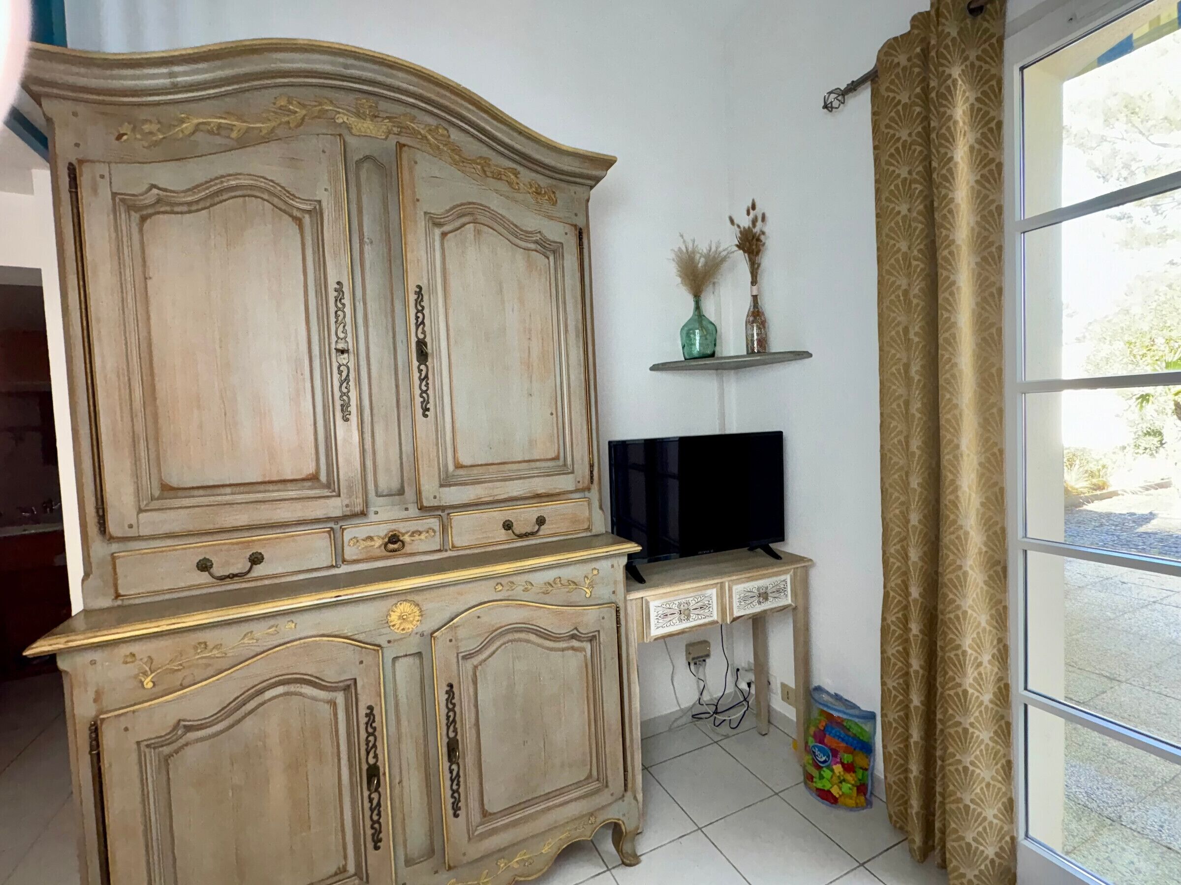 Een kamer met een grote houten kast, een televisie op een standaard en een raam met gordijnen.