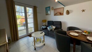 Una sala de estar con un sofá, una mesa de comedor con platos y vasos, una pequeña mesa blanca con botellas, una lámpara y una luz en el techo.