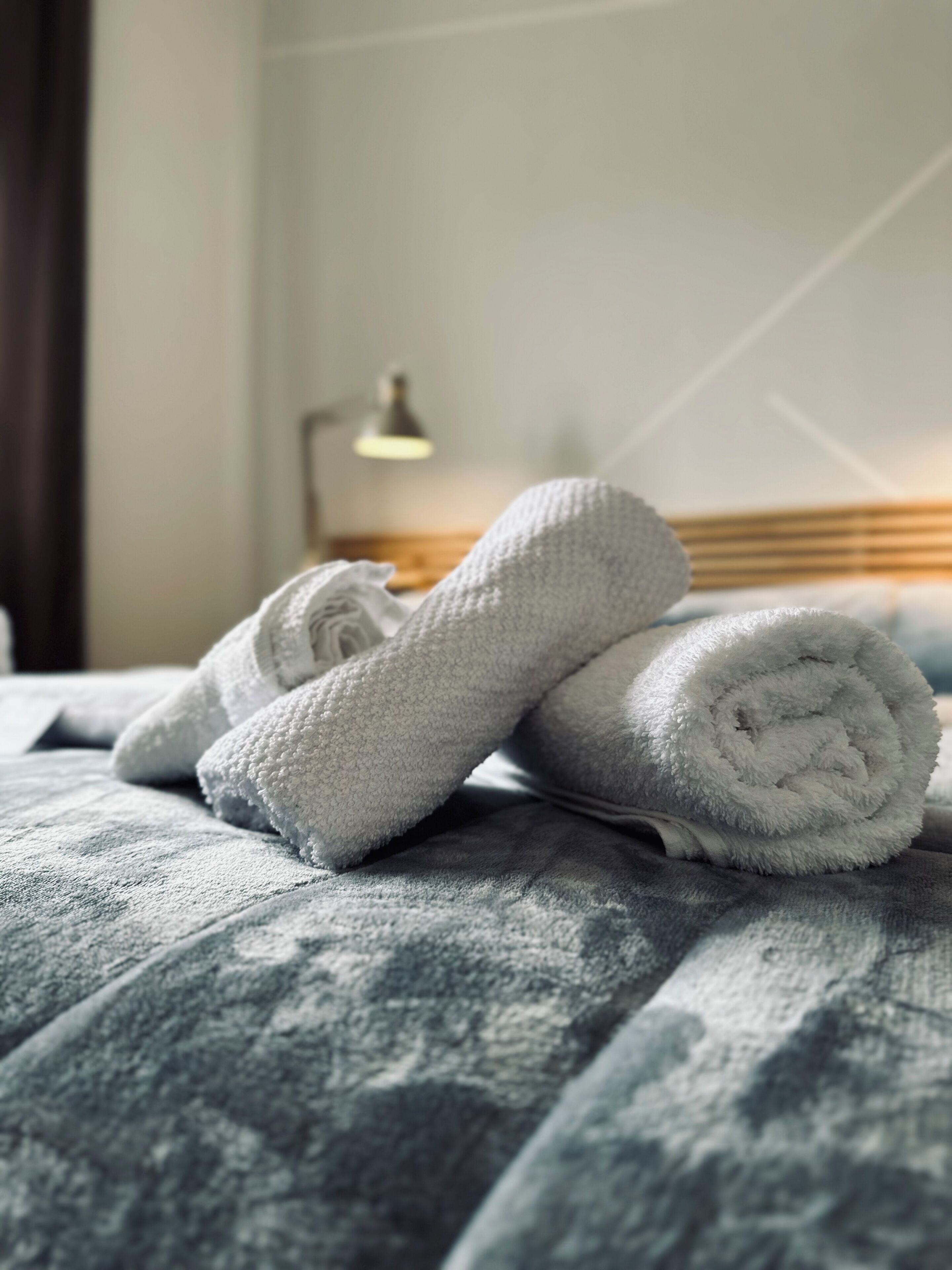 A neatly made bed with rolled white towels and a lamp in the background.