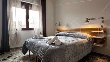 Un dormitorio con cama, mesita de noche, lámpara, ventana con cortinas y suelo de mármol.