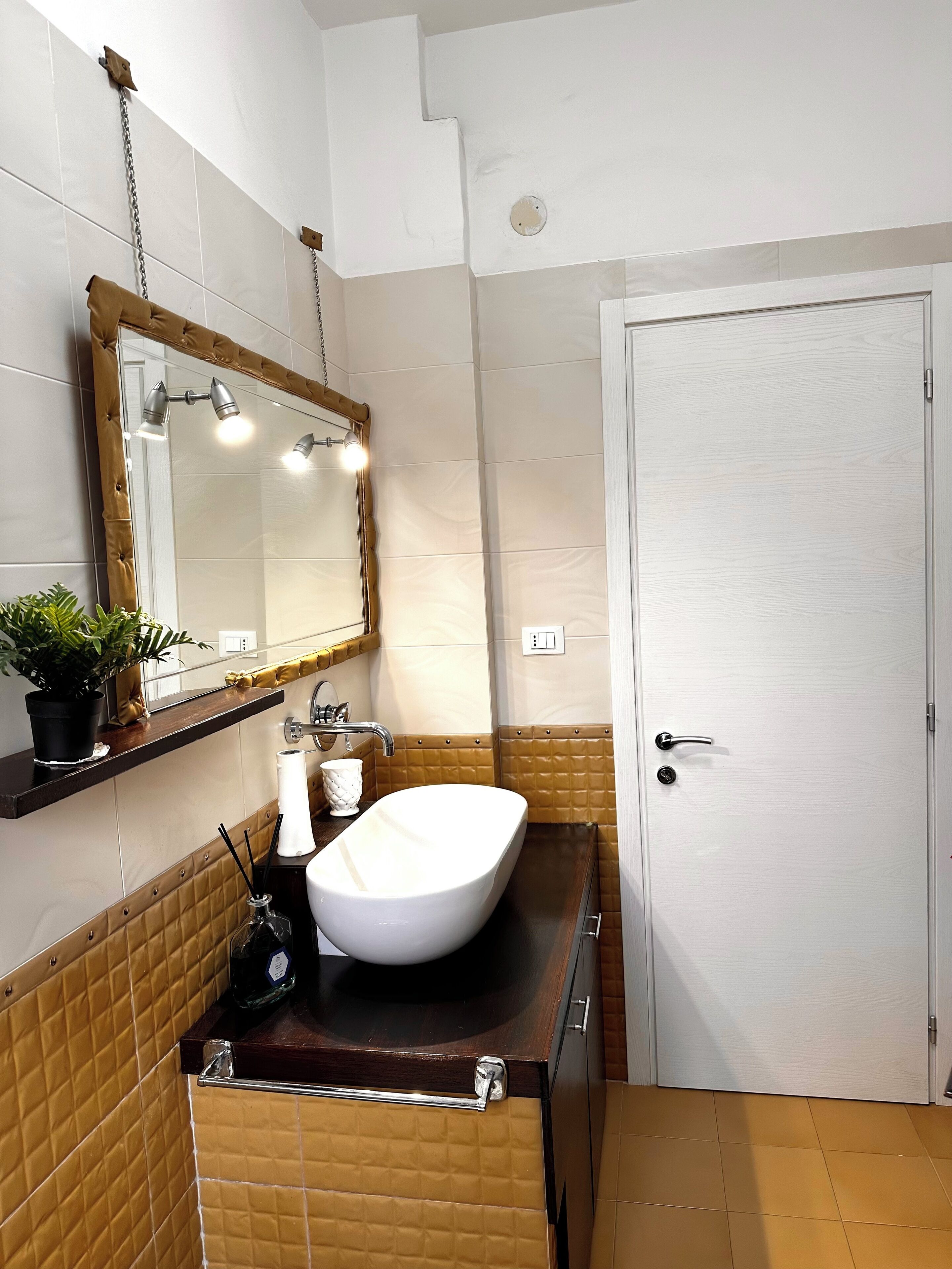 A bathroom with a white sink, a mirror with lights, a towel rack, and a door.