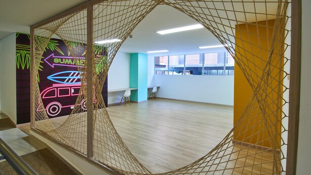 A spacious room with a wooden floor, a hammock, and a view of the sea through large windows.