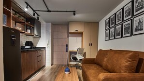 A modern kitchen with wooden cabinets, a coffee machine, and a dining area with a brown leather couch and a coffee table.