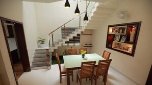 Un comedor con una mesa, sillas, una escalera y un estante en la pared con varios objetos.