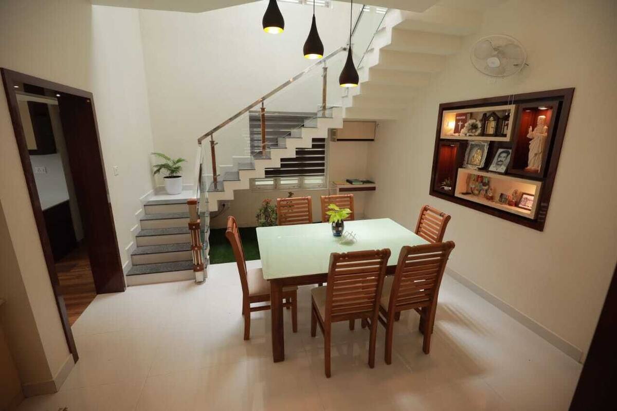 A dining area with a table and chairs, a staircase, and a wall-mounted shelf with various items.