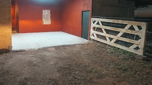 Un granero con piso de tierra, una verja de madera y una puerta roja.