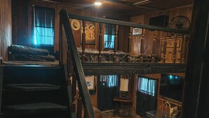 Una habitación rústica con una escalera de madera, una cama, una máquina de coser y un televisor.