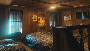 Una habitación tenuemente iluminada con paredes de madera, una cama con ropa de cama estampada, un televisor en la pared y un letrero que dice "BOER".